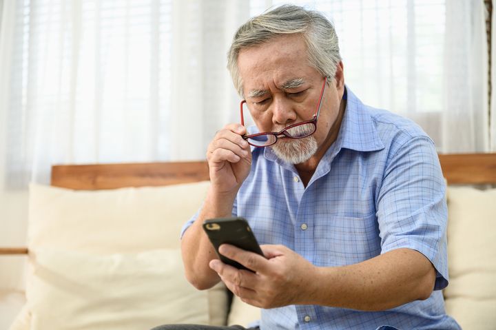 Man putting on spectacles as he looks at a mobile phone screen from a distance