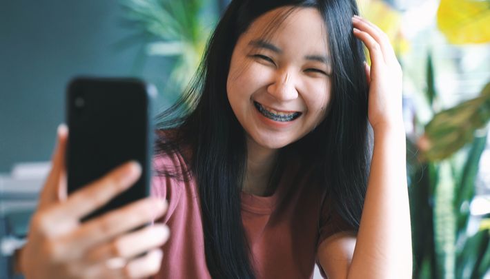 A young girl smiling happily and taking a selfie while touching her hair.