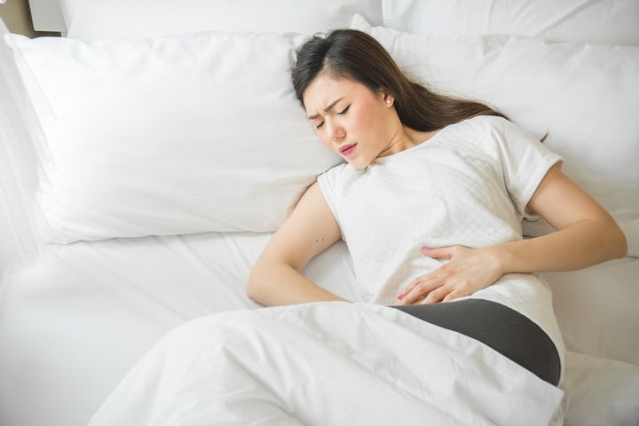 A woman holding her abdominal area in pain while lying in bed