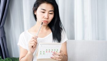 Woman staring at calendar noting her menstrual cycle.