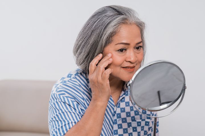 An older woman looks at a round mirror with a slight smile.