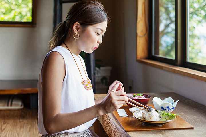 Woman picking up food from a plate using chopsticks as she sits at a wooden table