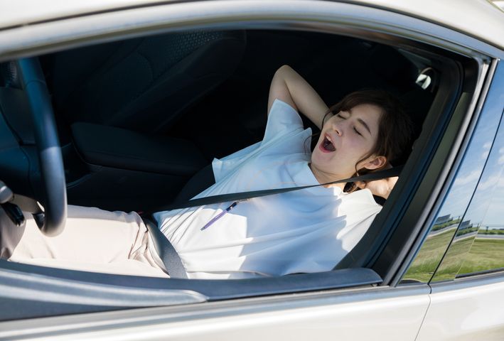 A woman yawning while lying back on her seat inside a car.