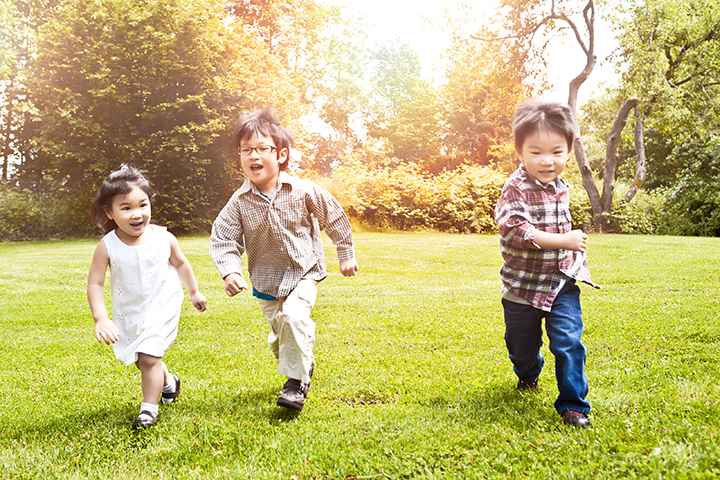 Three children running in a park while the sun shines