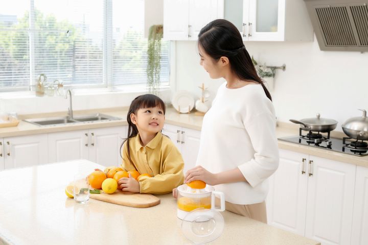 A mother and daughter making freshly-squeezed orange juice in the kitchen.