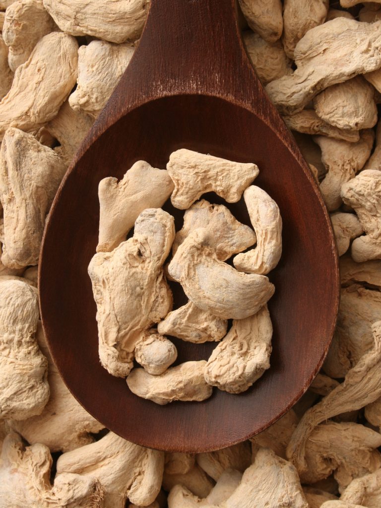 Top view of wooden spoon full of dried ginger roots