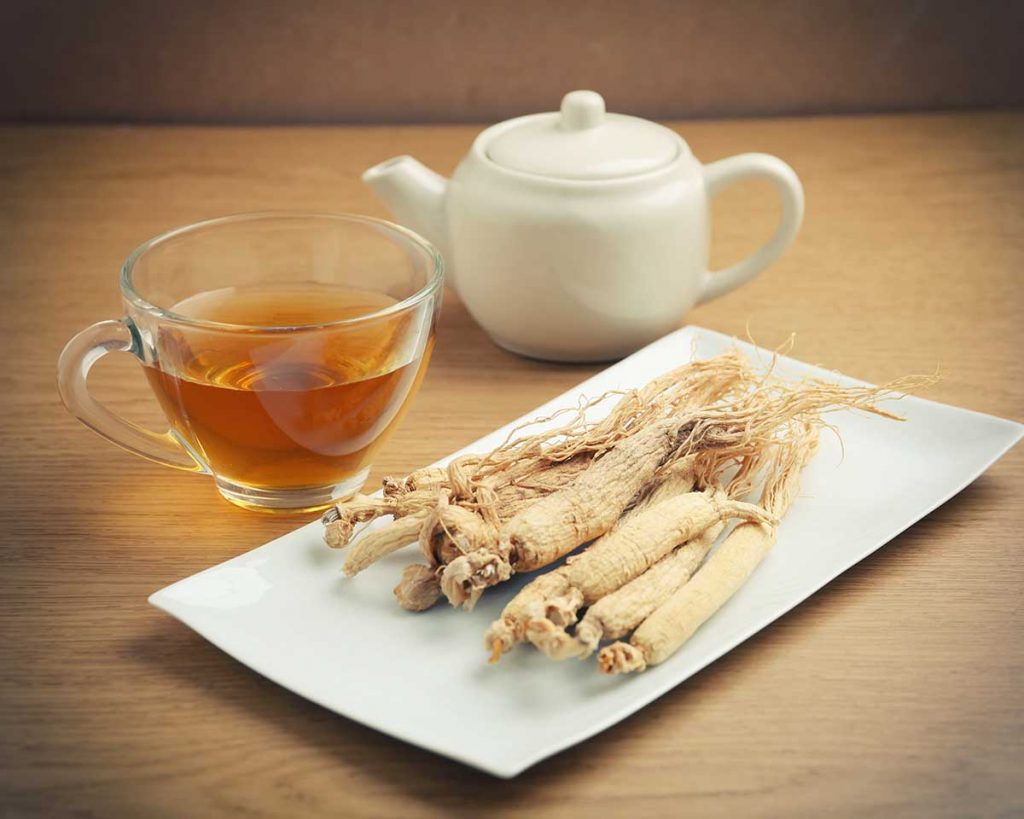 Dried ginseng roots, a cup of ginseng tea, and a teapot on a wooden table