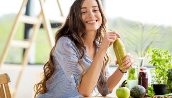 Beautiful happy woman sitting with drinks and healthy green food at home