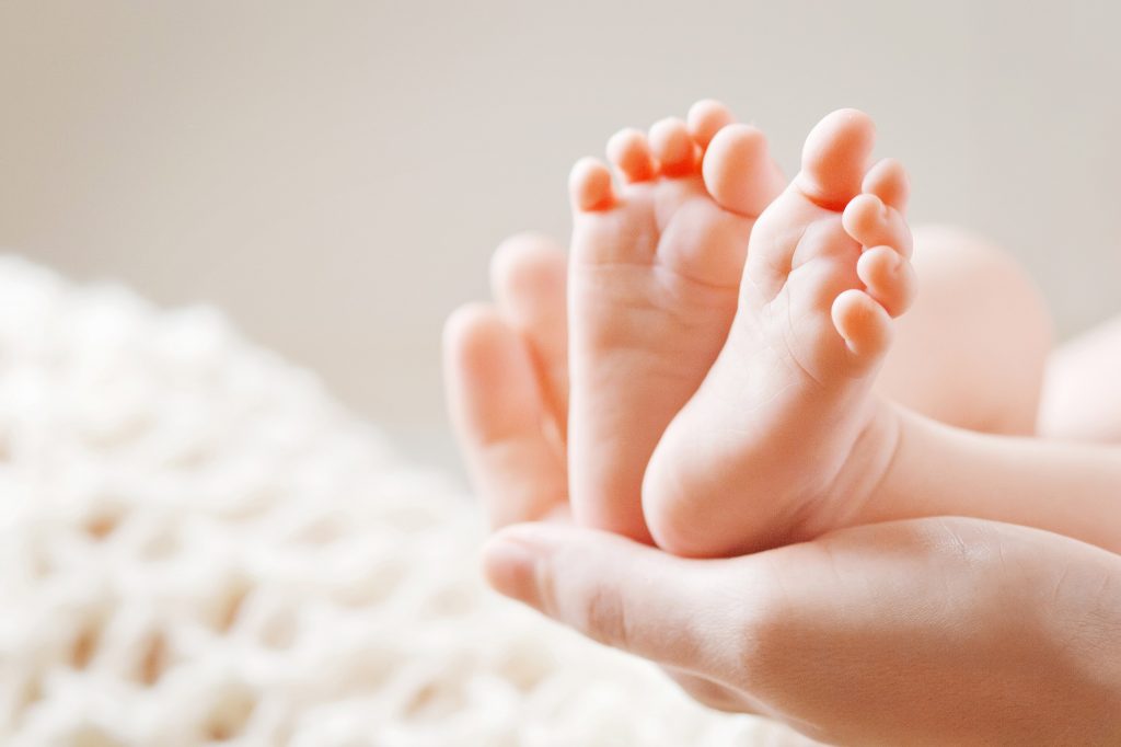 Tiny baby feet in mother's hands with blurry beige background