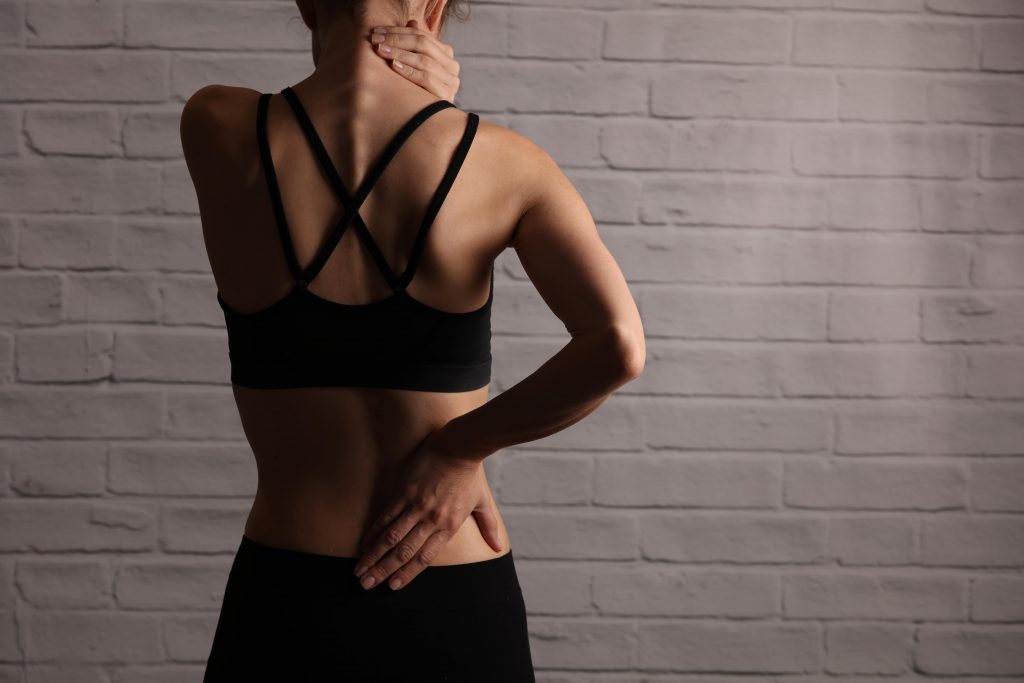 Woman wearing a workout gear in need of pain relief, touching her neck and lower back