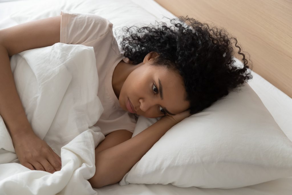 Pensive African American woman lying in bed awake