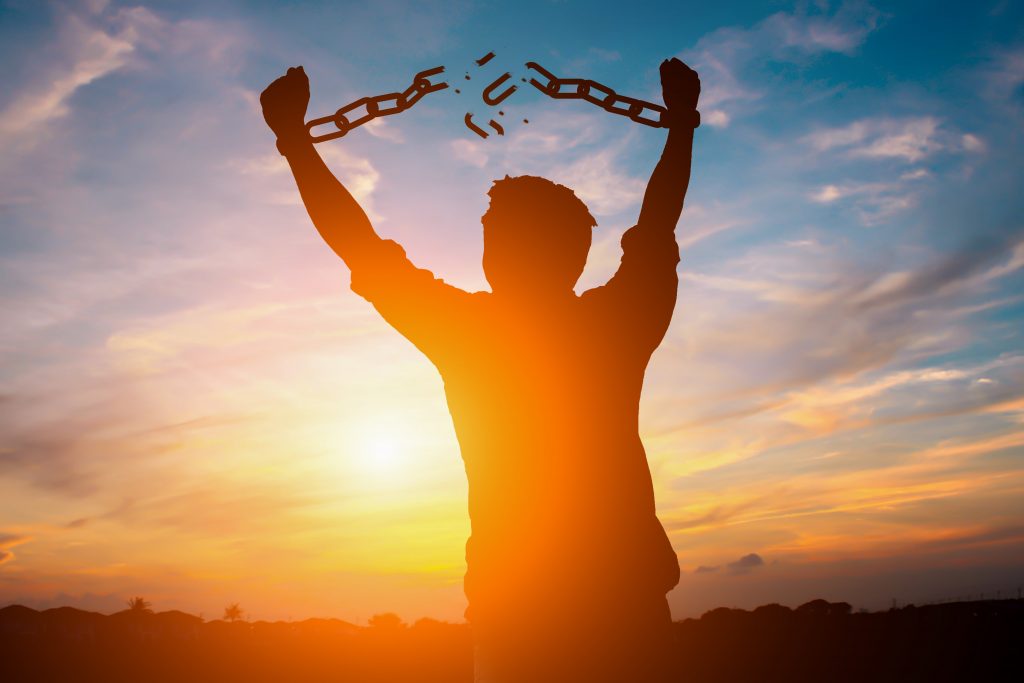 Man silhouetted against a bright sunny sky breaking free of chains around his wrists