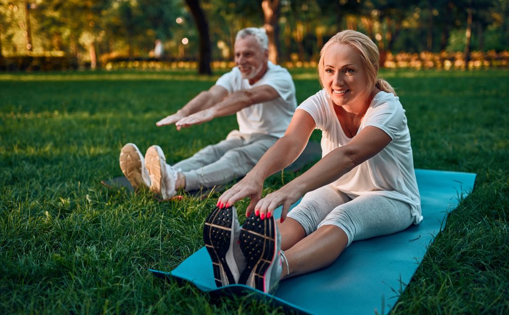 a senior couple stretching on a grass in a park