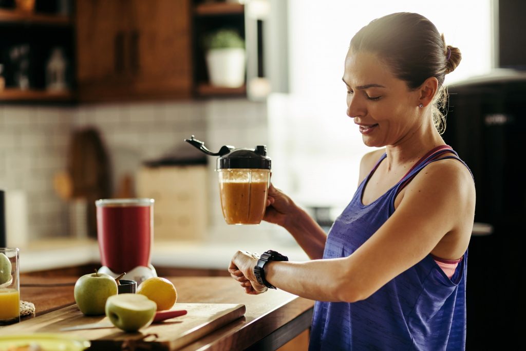 A woman drinking smoothie looking at her wristwatch