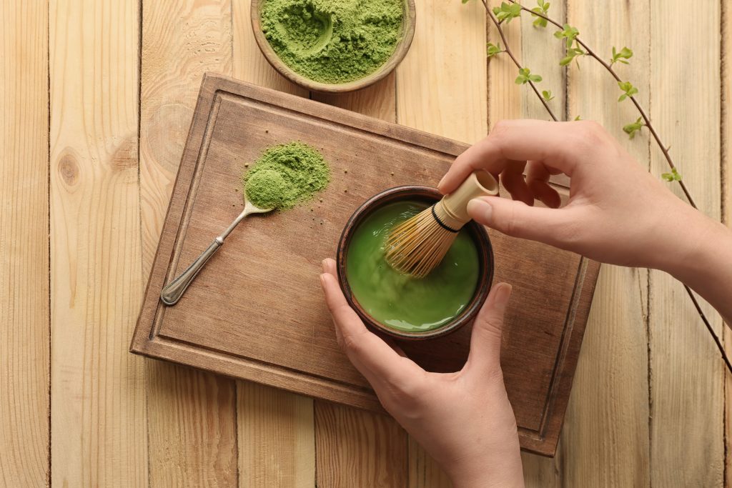 A person making green tea with matcha powder in a wooden cup