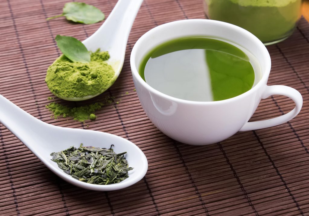 Getting the green tea benefits. A cup of green tea next to ground tea leaves and green tea powder