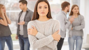 An anxious woman wearing grey sweater stand alone in a crowd