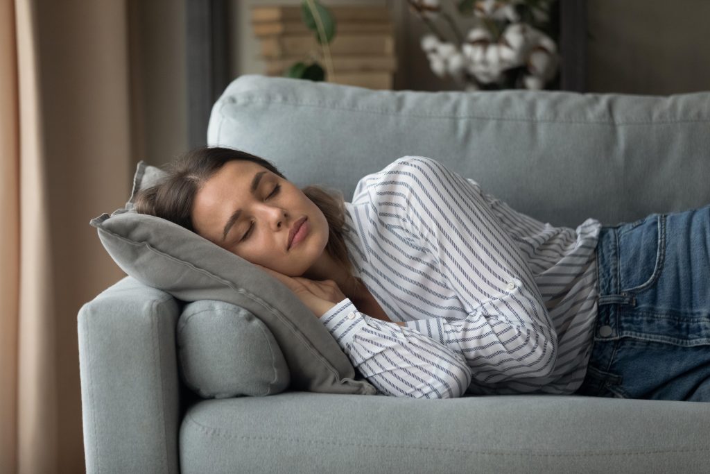 A woman wearing white shirt sleeping on a sofa in the afternoon