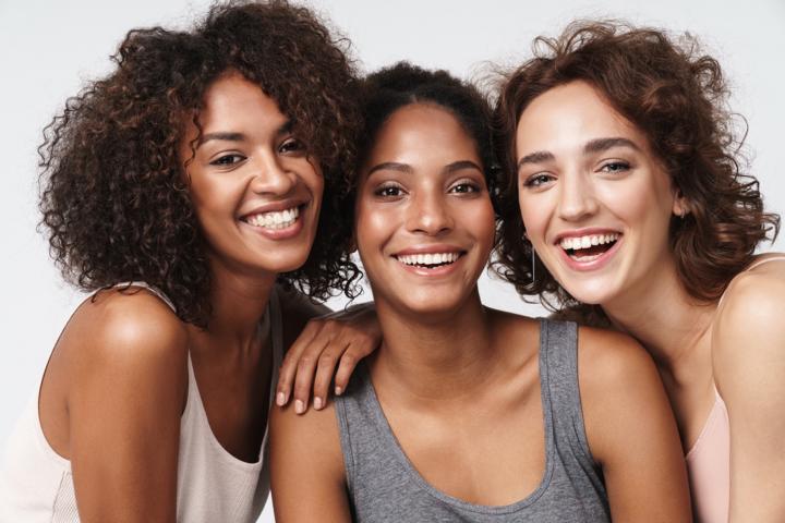 Three beautiful women of various ethnicities smiling and posing together in front of the camera
