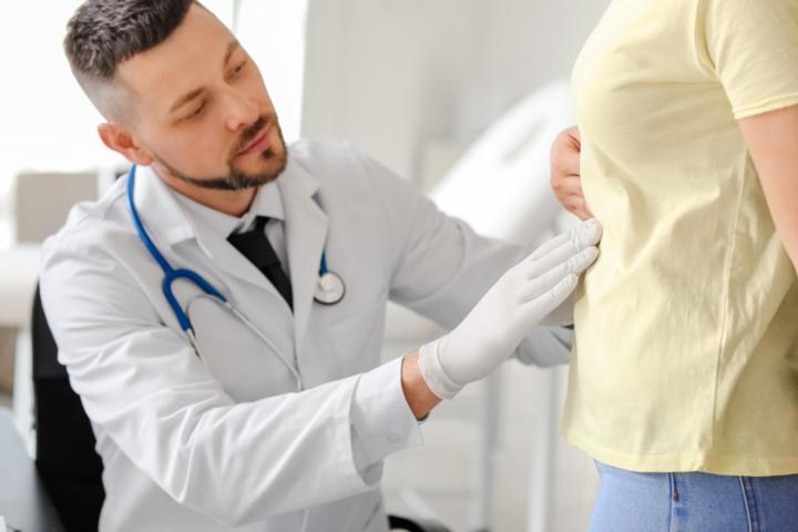A male doctor observing the abdominal area of a woman patient in the clinic