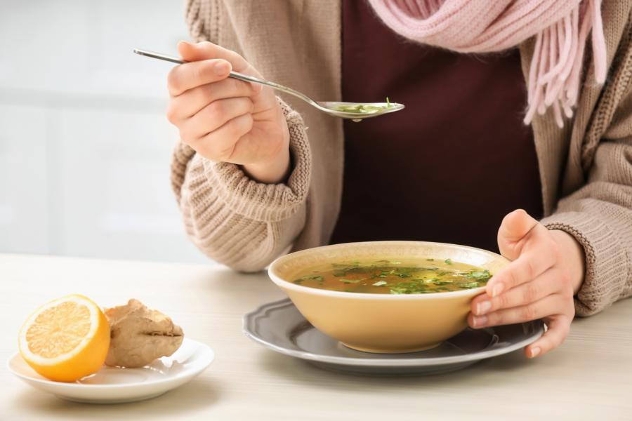 A sick woman eating herbal soup made with ginger and a dash of lemon to get rid of her flu symptoms