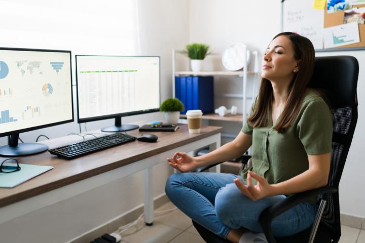 A young woman meditating in front of her computer screens as she is working during the day