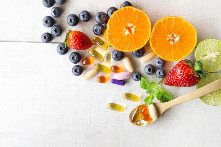 Supplements and fresh fruits for immune system booster are spread out over a table.