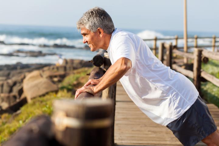 A white senior man with gray hair exercising outdoor on a beach