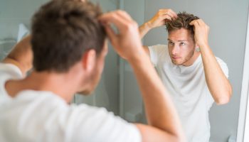 A young Caucasian man touching his hair in front of the mirror