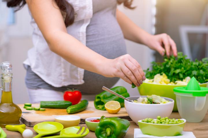 Pregnant woman preparing a meal with lots of vegetables