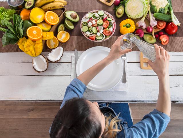 A woman pouring herself a glass of water as she begins to eat healthy meal of vegetables and fruits
