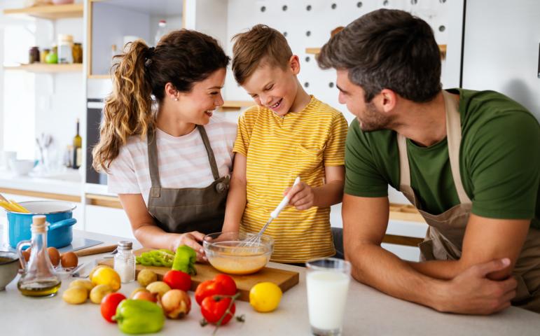 A family of three is cooking a healthy meal in the kitchen together.