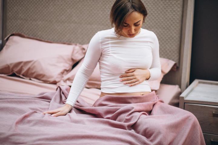 A pregnant woman in her first trimester holding her stomach at the side of the bed due to her hyperemesis gravidarum