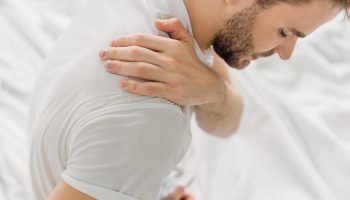A man touches his shoulder in pain due to muscle fatigue