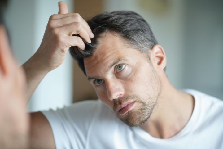 A middle age man touching his grey salt and pepper hair in the mirror
