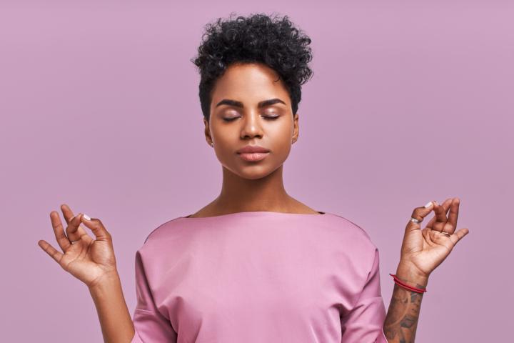 A woman wearing purple blouse is meditatin with purple background behind her