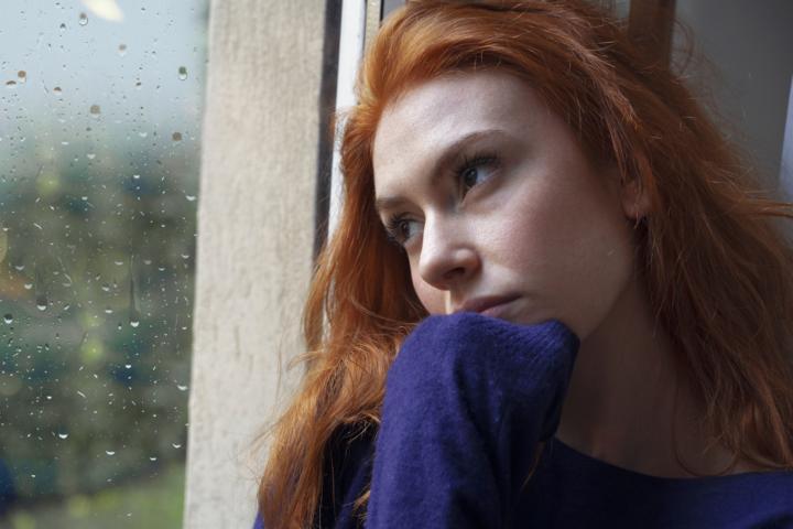 A woman looking sad while looking at rain droplets from her window