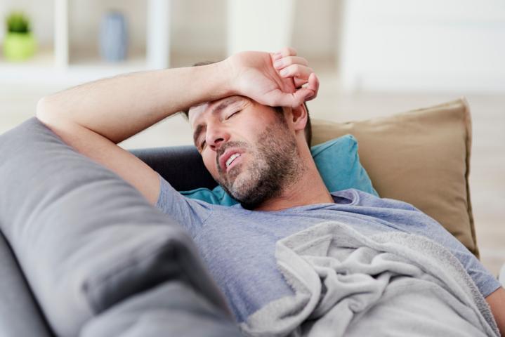 A man having a fever is laying down on a sofa while touching his forehead